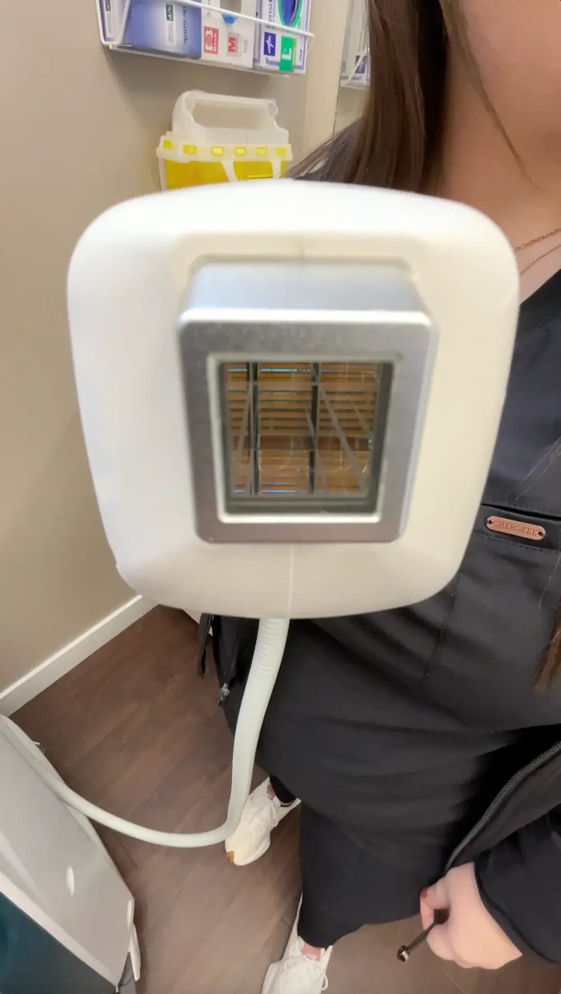 close-up-of-laser-device-held-by-technician-in-treatment-room-laser-hair-removal-saskatoon-equipment-with-cooling-hose-visible-floor-and-supplies-in-background-1