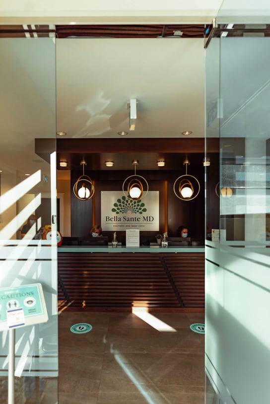 glass-entrance-view-of-bella-sante-md-reception-area-with-staff-sitting-behind-the-front-desk
