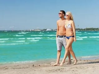 man-and-woman-in-swimwear-walking-along-sandy-beach-with-turquoise-waves-and-clear-sky-in-background