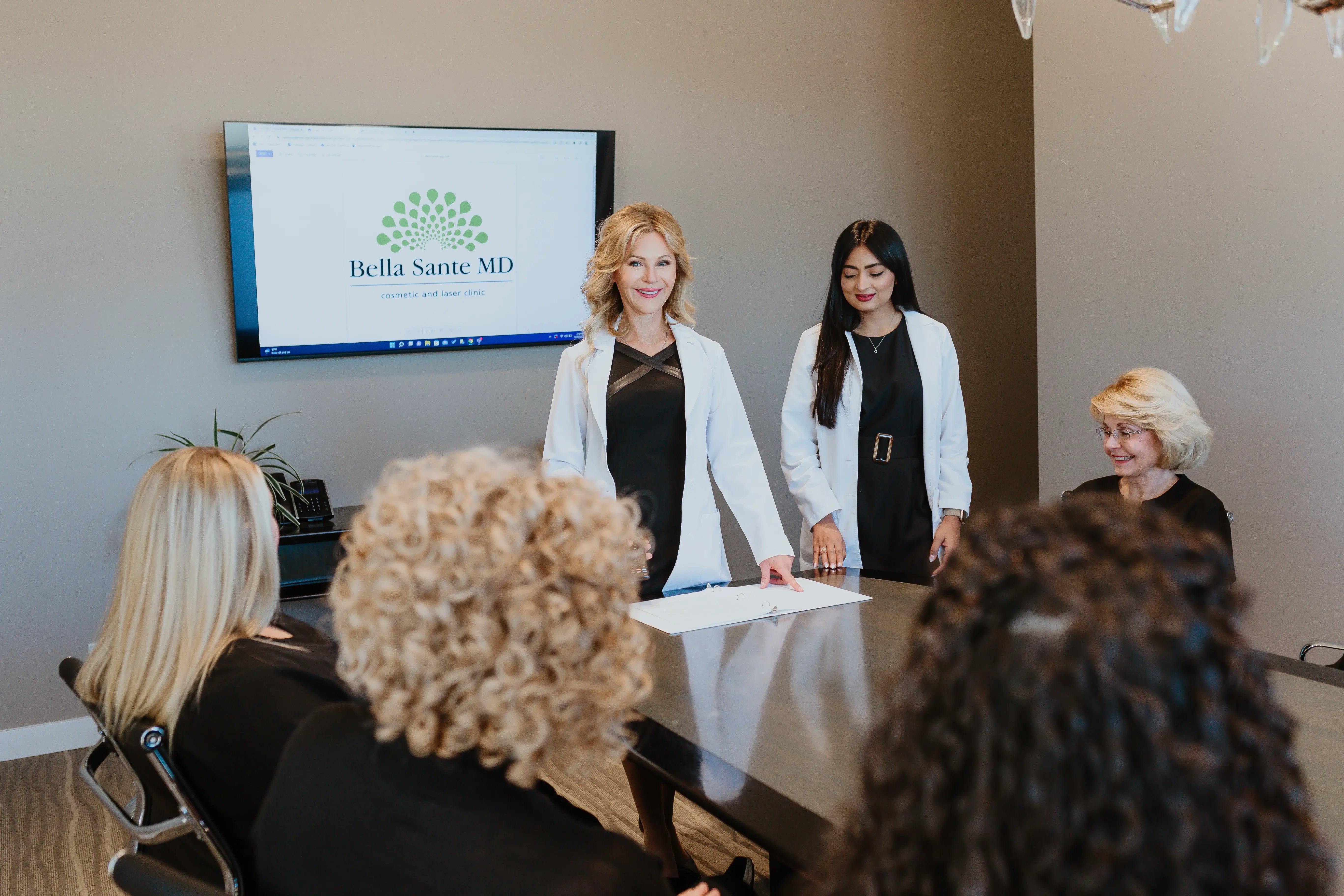 medical-team-standing-at-table-addressing-seated-group-with-bella-sante-md-logo-on-screen