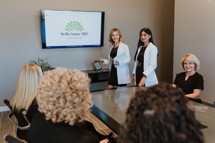 team-of-medical-professionals-in-white-coats-presenting-in-conference-room-with-bella-sante-md-logo-on-screen-while-staff-members-listen-attentively