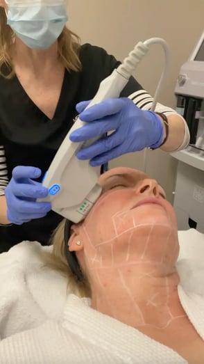 technician-wearing-blue-gloves-and-mask-performing-ultrasound-treatment-on-patient-face-and-neck-with-white-marking-lines-visible