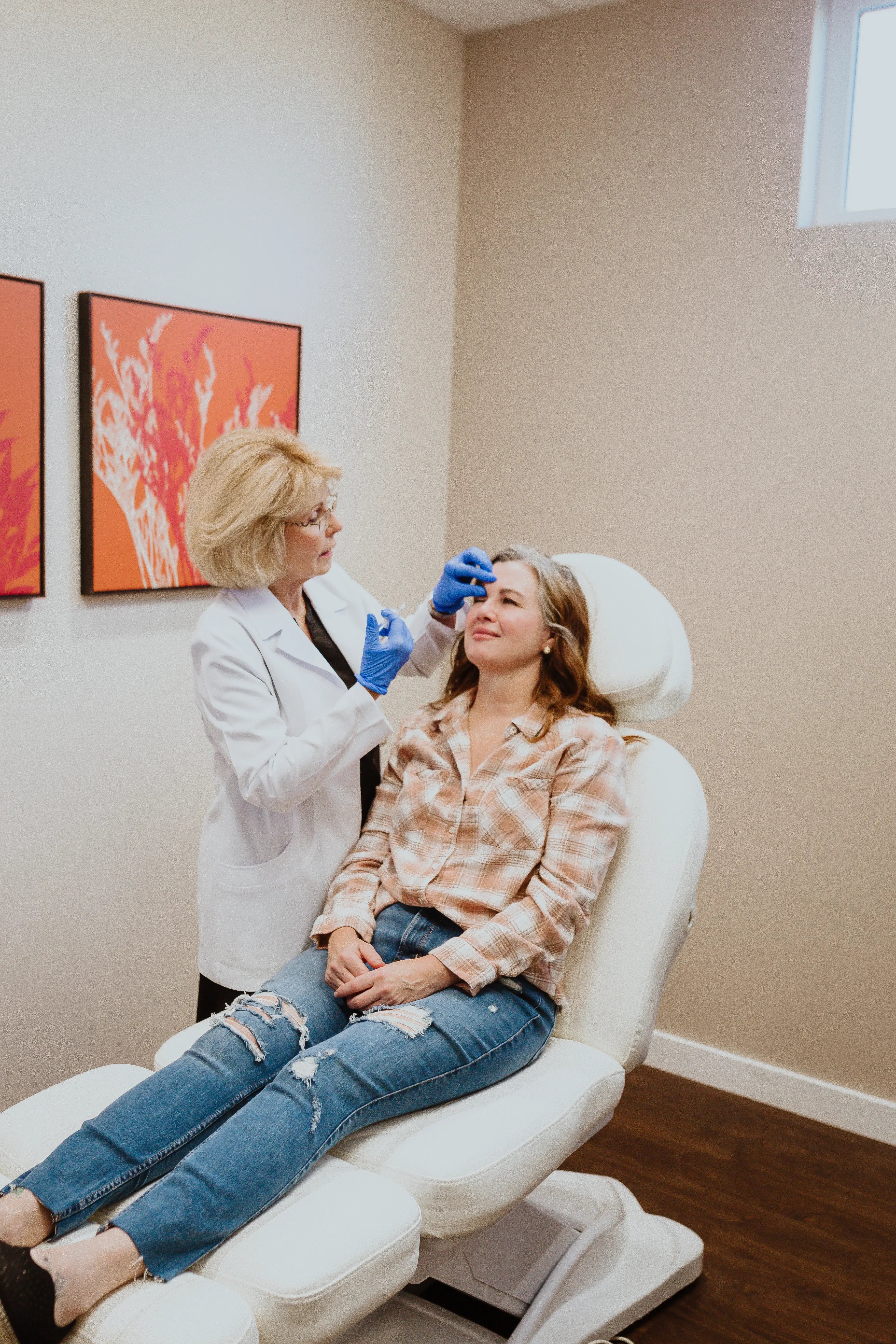 woman-sitting-in-treatment-chair-while-provider-in-white-coat-and-blue-gloves-examines-her-forehead-discussing-pros-and-cons-of-sculptra-during-a-consultation